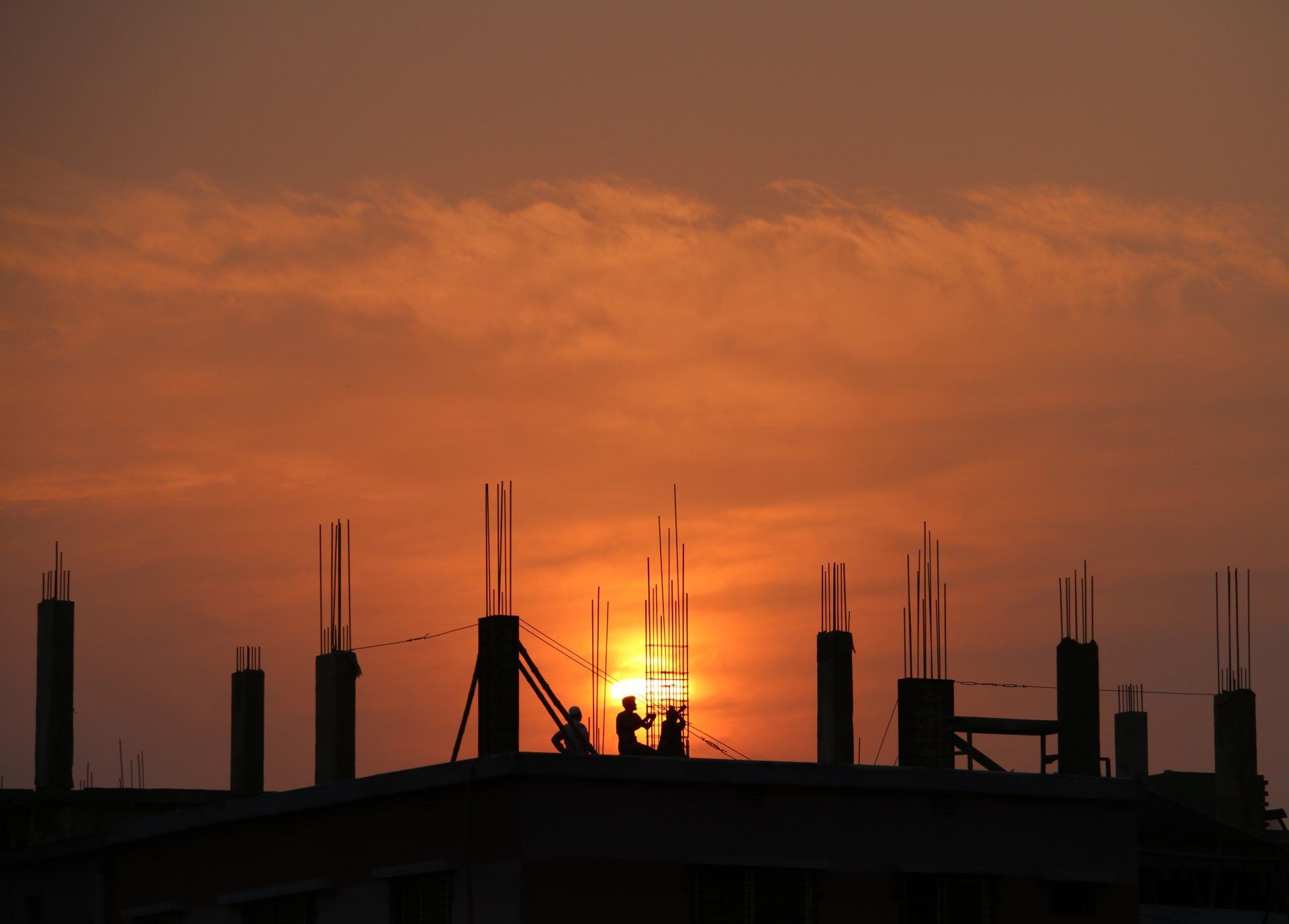 A group of construction workers are standing on top of a building at sunset.